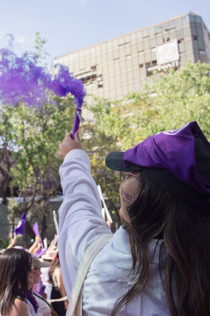 feminist-protest-in-mexico-city-displaying-purple-smoke-31227624 A vibrant feminist march in Mexico City with participants waving purple flags and smoke flares.